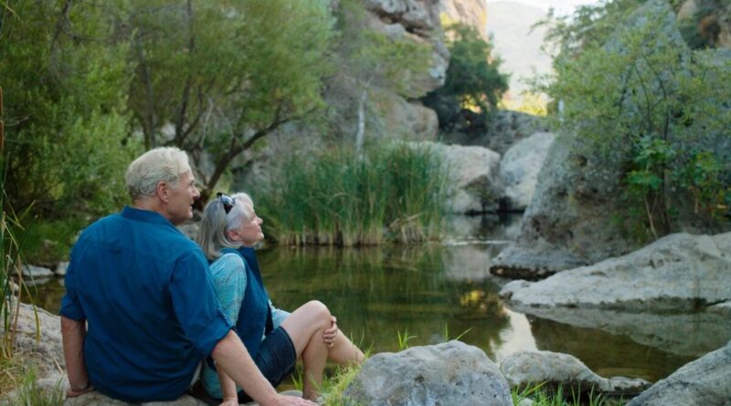 Two people sitting on the shore of a river